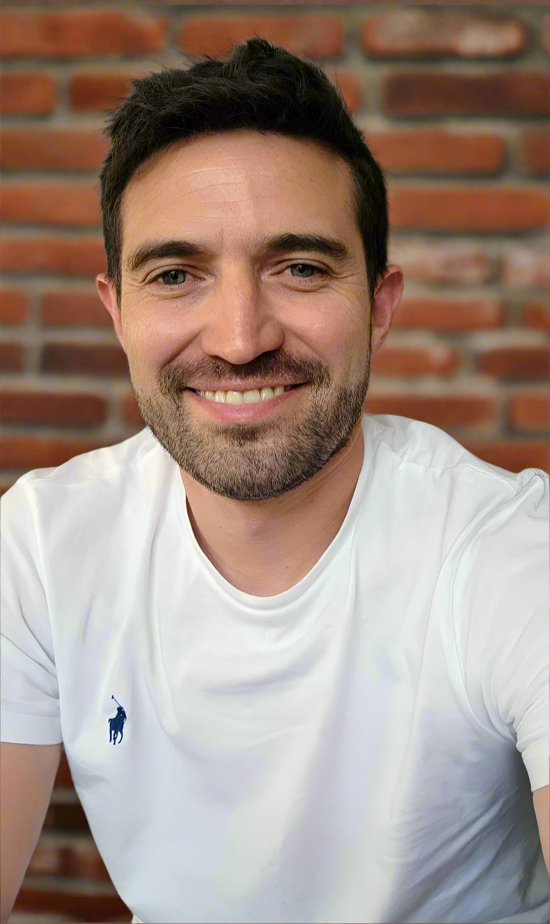 Man wearing a white t-shirt with a logo against a brick wall Ashley Perry