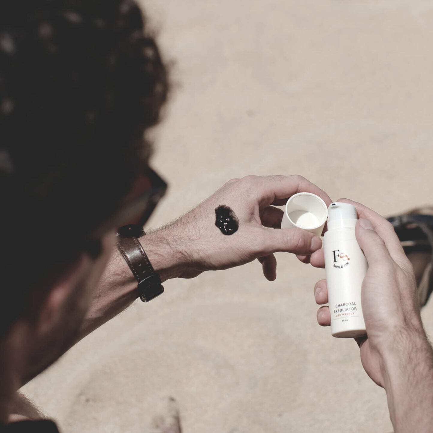 Person applying charcoal exfoliator from a bottle onto their hand.