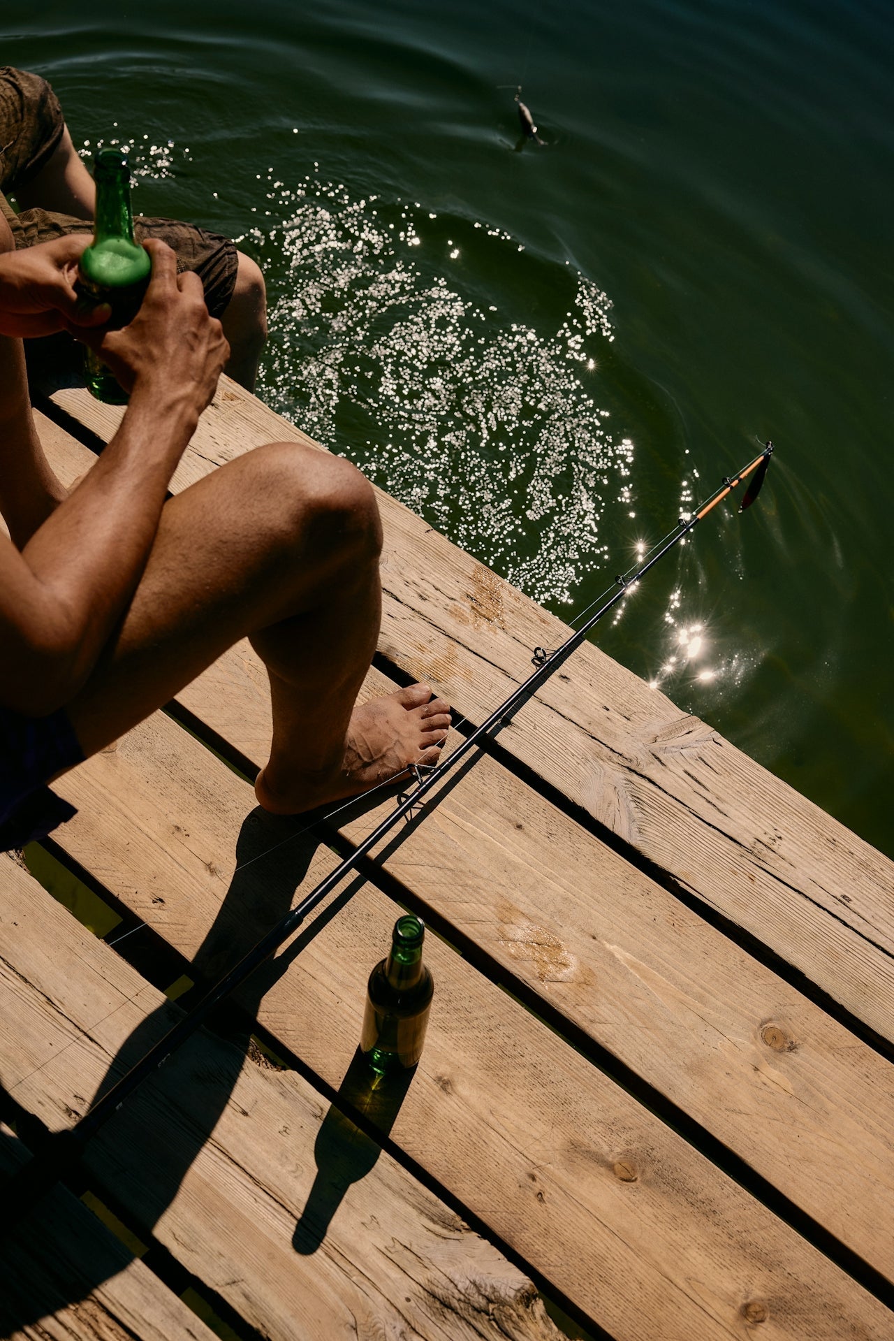 men chilling by the water with a beer and fish rod in the sun