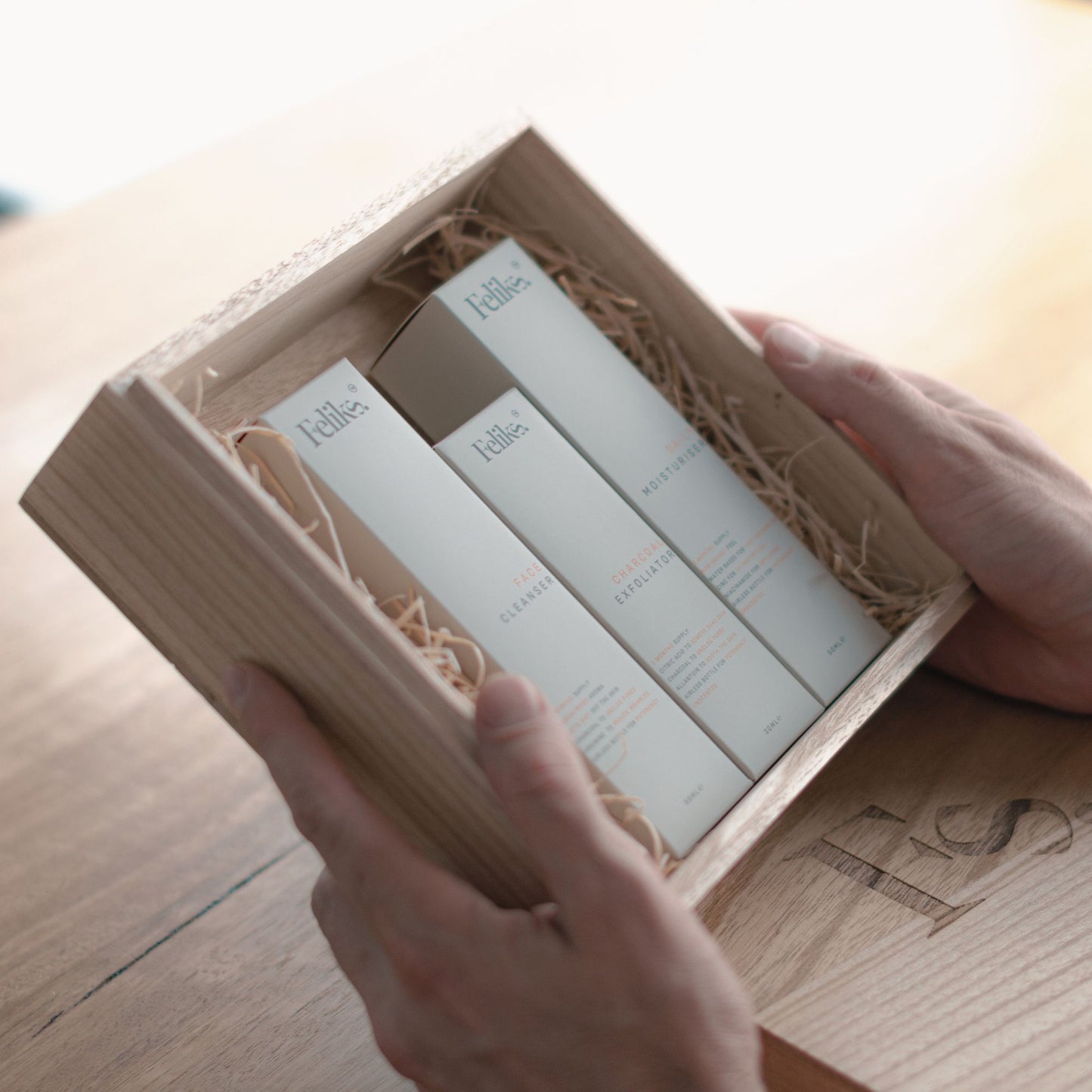 The image shows the Feliks skincare gift box held in a man's hands. The gift box is wooden. Inside the gift box are three boxes of mens skincare including cleanser, exfoliator and moisturiser.
