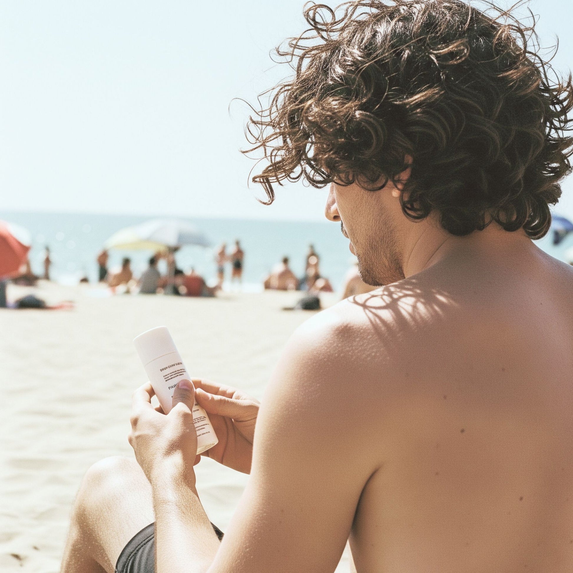 Man holding Feliks SPF Moisturiser on a beach with people and umbrellas in the background