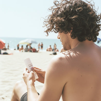 Man holding Feliks SPF Moisturiser on a beach with people and umbrellas in the background